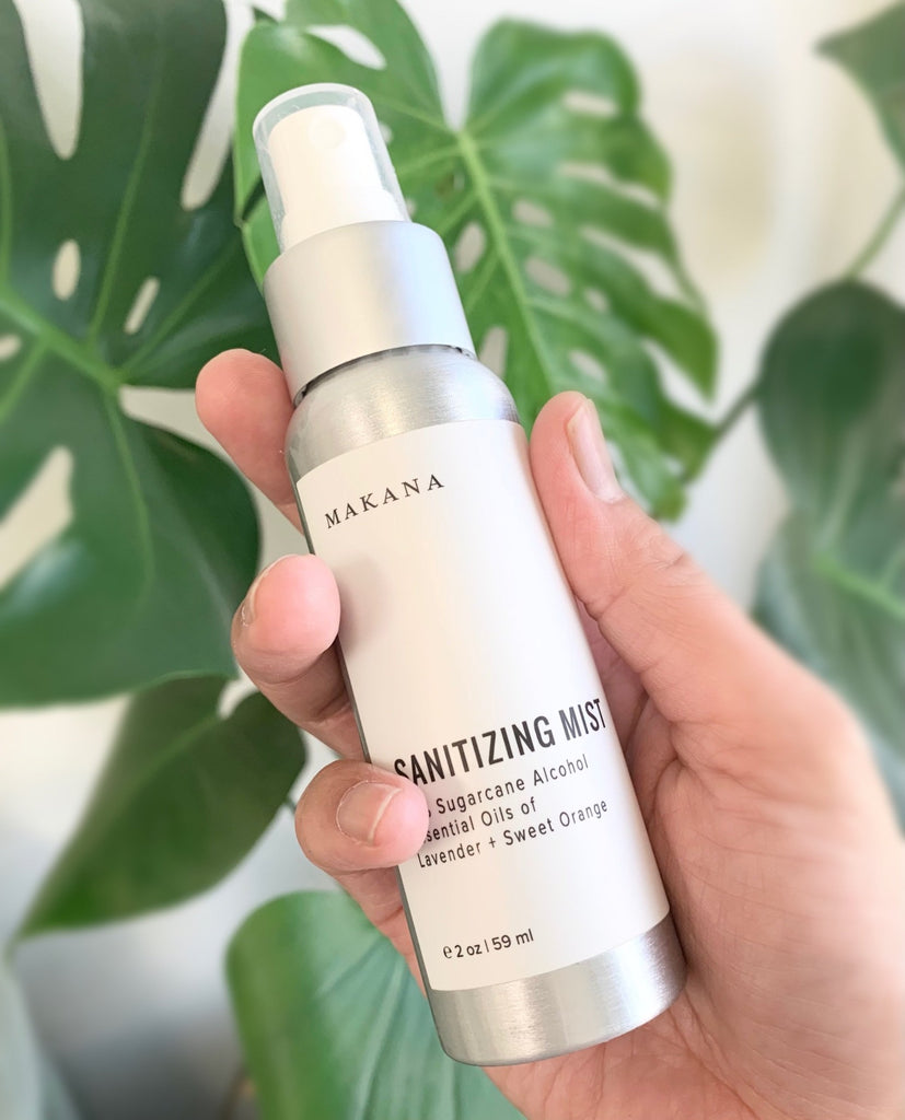 a hand is holding a silver aluminum bottle of hand sanitizer with plants in the background